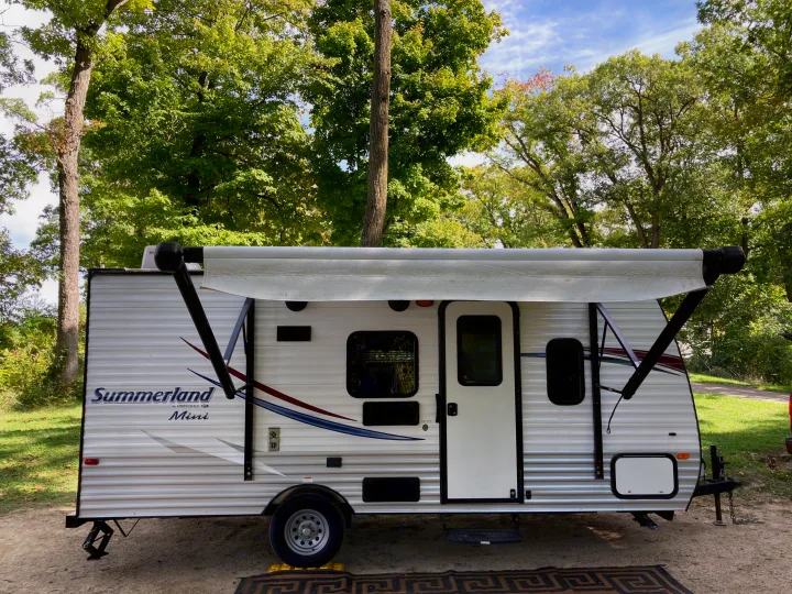 Summerland Mini RV rental at a serene campsite, nestled among green trees. Ideal for outdoor travel.. Keystone RV Summerland Mini 2016