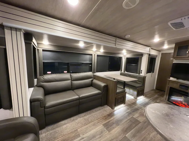 This RV rental interior shows a gray sofa, dinette with table, and a fireplace, creating a modern, cozy living space.. Keystone Cougar Half-Ton 2021