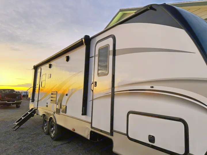 Golden sunset light reflects on a parked white Cougar RV rental. This large travel trailer features extended entry steps and a pickup truck.. Keystone Cougar Half-Ton 2021