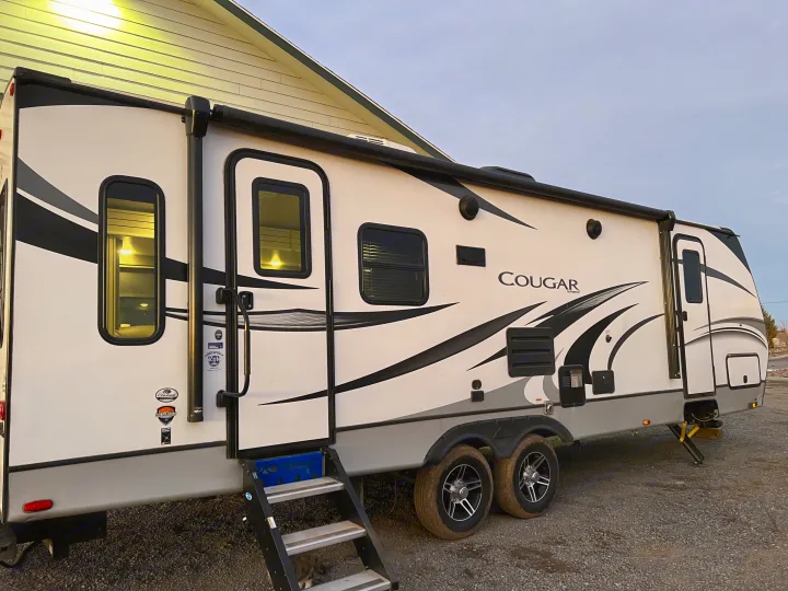 White Cougar travel trailer with steps down and awning, parked on gravel. Ideal for your next RV rental.. Keystone Cougar Half-Ton 2021