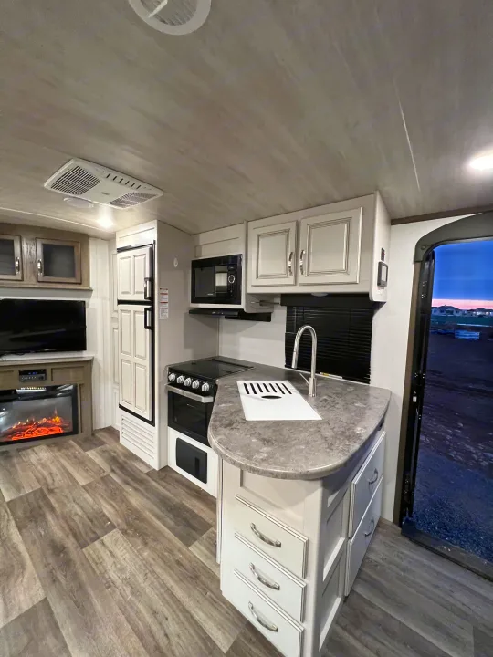 Modern RV rental interior: well-appointed kitchen with stove, microwave, and sink, plus a living space with TV and fireplace.. Keystone Cougar Half-Ton 2021