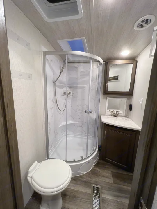 Compact RV rental bathroom with a corner shower, toilet, and sink vanity, designed for comfortable travel.. Keystone Cougar Half-Ton 2021