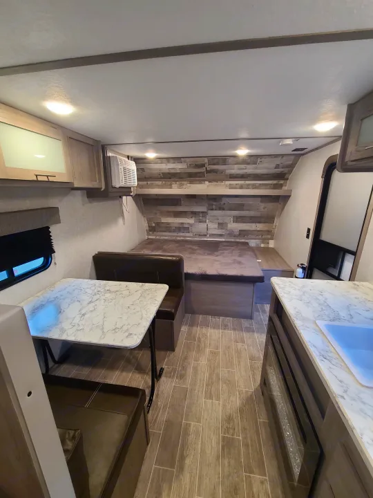 Bright RV rental interior featuring a versatile dining space, comfortable bed, and essential kitchen counter. Ideal for travel.. Coleman Latern 17b 2022
