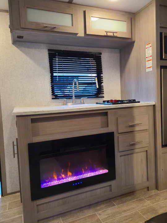 Spacious RV rental interior: modern kitchen with sink, stovetop, ample cabinets, and a cozy electric fireplace.. Coleman Latern 17b 2022