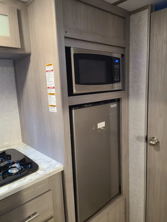 Compact RV rental kitchenette featuring a microwave, mini-fridge, and two-burner stovetop, ideal for travel.. Coleman Latern 17b 2022