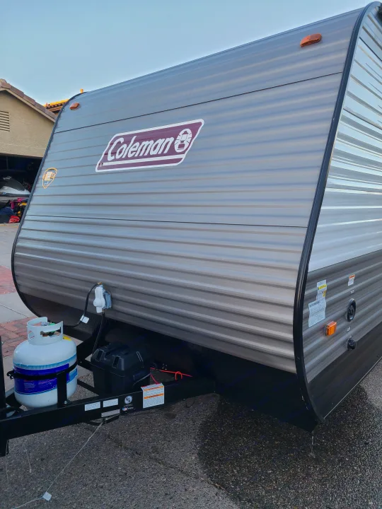 Coleman travel trailer RV rental, front view with propane tank, battery, and ribbed gray siding on a paved surface.. Coleman Latern 17b 2022