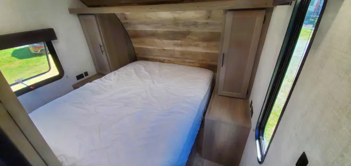 Cozy RV rental bedroom showing a comfortable bed, rustic wood wall, side storage, and windows for natural light.. Gulf Stream Trailmaster 2021