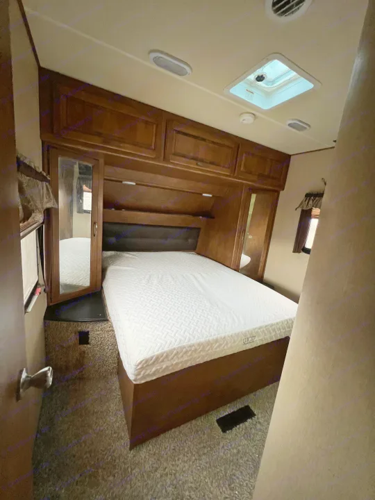 Step into this inviting RV rental bedroom, featuring a comfortable white bed, wooden storage, and a ceiling skylight.. Grand Design Reflection 2015