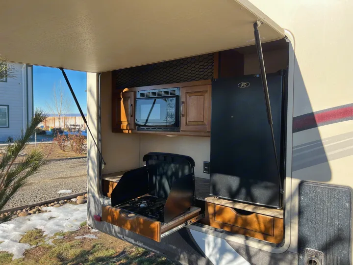 An RV rental's opened hatch reveals a full outdoor kitchen with microwave, fridge, and pull-out stove for camping.. Grand Design Reflection 2015