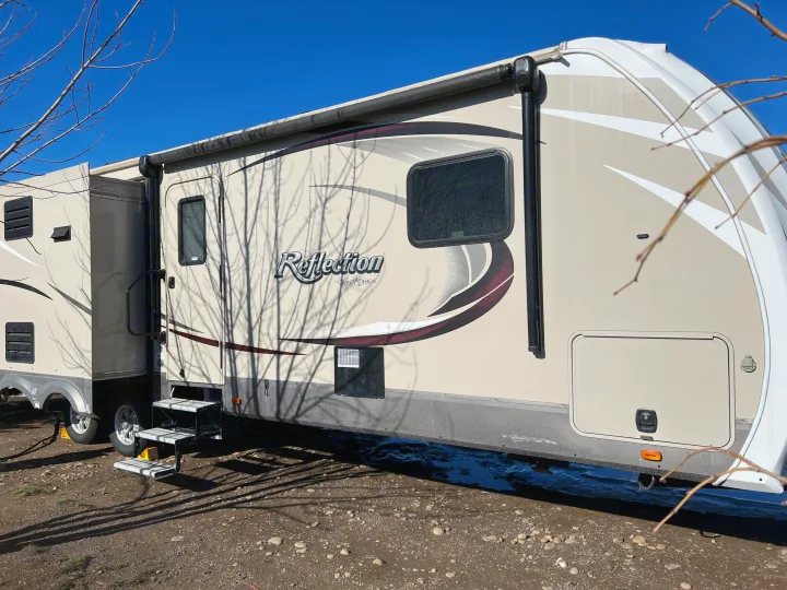 Spacious beige fifth-wheel RV rental, with multiple windows and slide-outs, parked outdoors on a sunny day.. Grand Design Reflection 2015