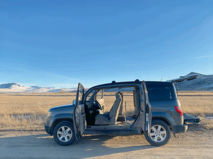A versatile Honda Element with all doors open, parked in a scenic mountain field, ready for a road trip. Great RV rental alternative.. Honda Element 2009