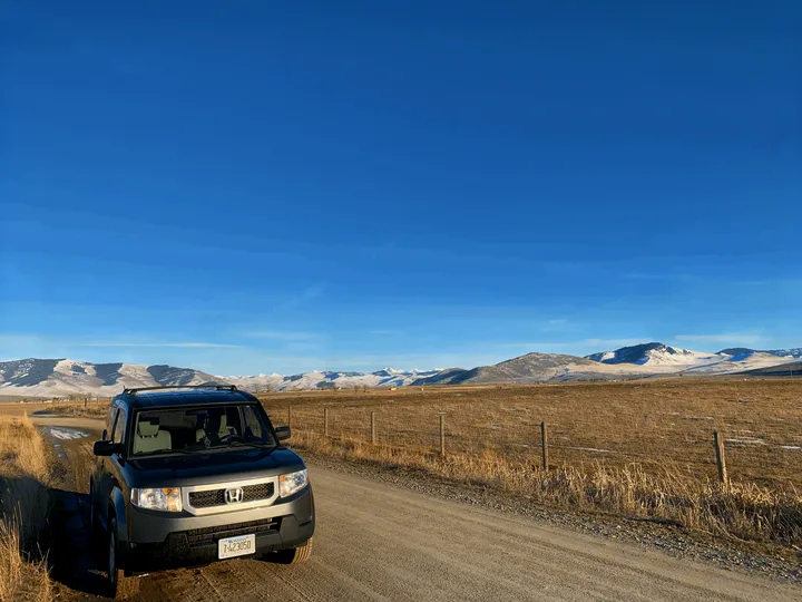 Honda Element on a Montana dirt road with snowy mountains. Experience similar vast landscapes with an RV rental.. Honda Element 2009