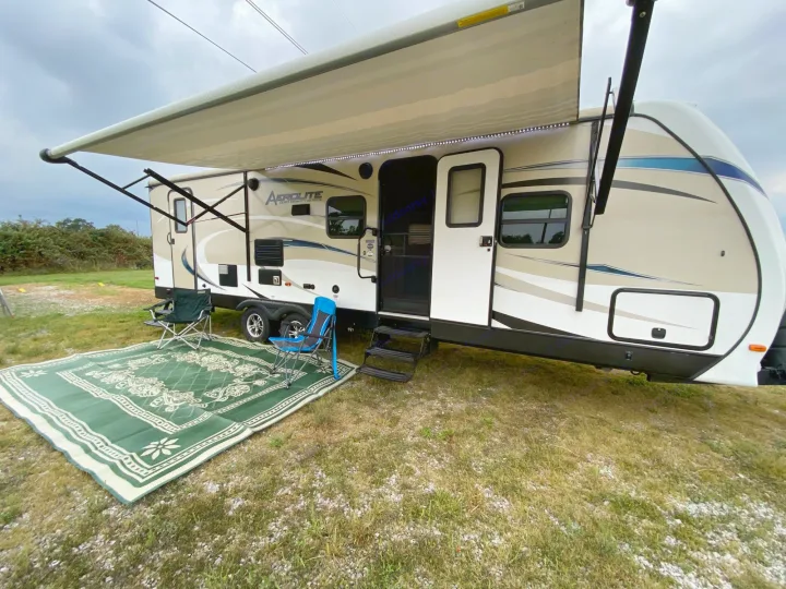 This RV rental shows a travel trailer with an extended awning, outdoor mat, and camping chairs set up on grass.. Dutchmen Aerolite 2017