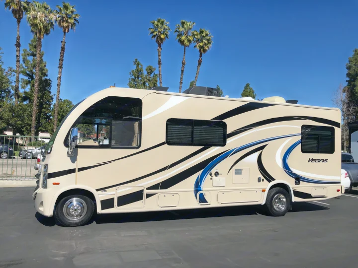 Tan Class C RV rental with 'VEGAS' logo and graphic accents, parked on asphalt under a blue sky with palm trees.. Thor Vegas 2017