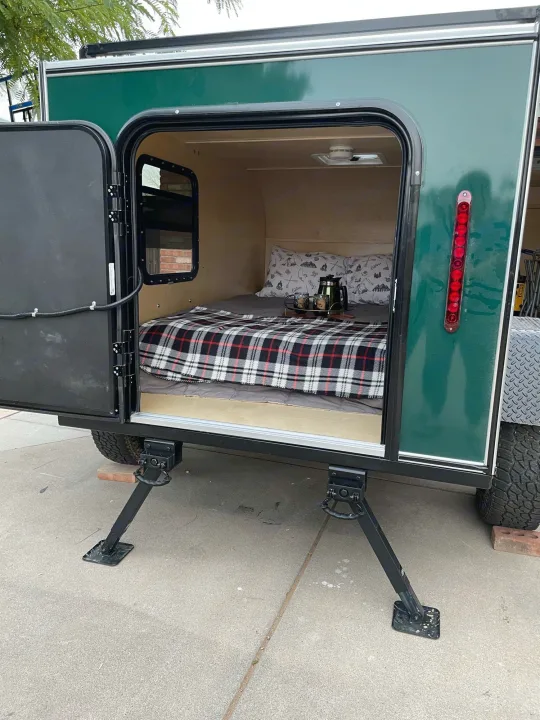 Cozy green teardrop RV rental ready for adventure. Open door reveals comfy bed with plaid blanket. Perfect for camping.. Other Other 2022