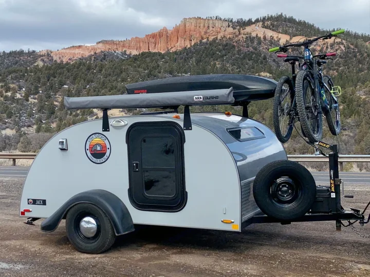 An RV rental teardrop camper with bikes and a roof cargo box sits ready for adventure amidst Utah's red rock mountains.. Little Guy Silver Shadow 2015