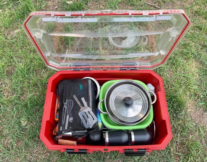 A red outdoor case open on grass, revealing neatly packed camping cooking gear: pots, utensils, and mugs. Ideal for your RV rental adventure!. Little Guy Silver Shadow 2015
