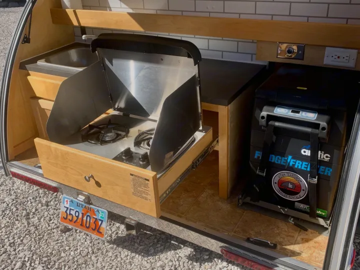 Explore this RV rental's teardrop trailer kitchen, featuring a pull-out stove, sink, and fridge, ideal for mobile camping.. Little Guy Silver Shadow 2015