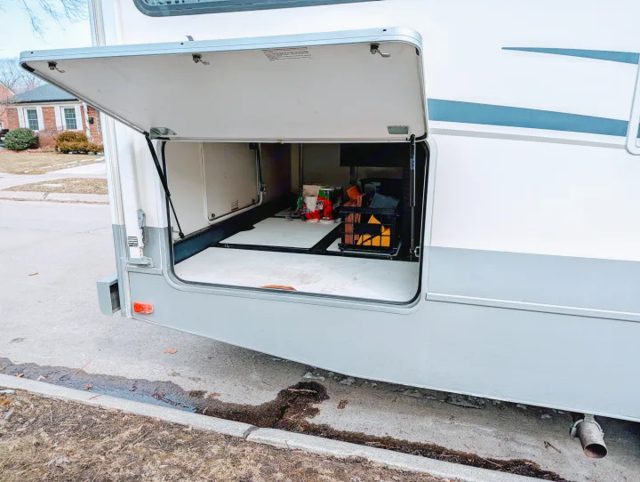 Side view of an RV rental with its large exterior storage bay open, revealing various travel supplies inside.. Fleetwood Tioga 2005
