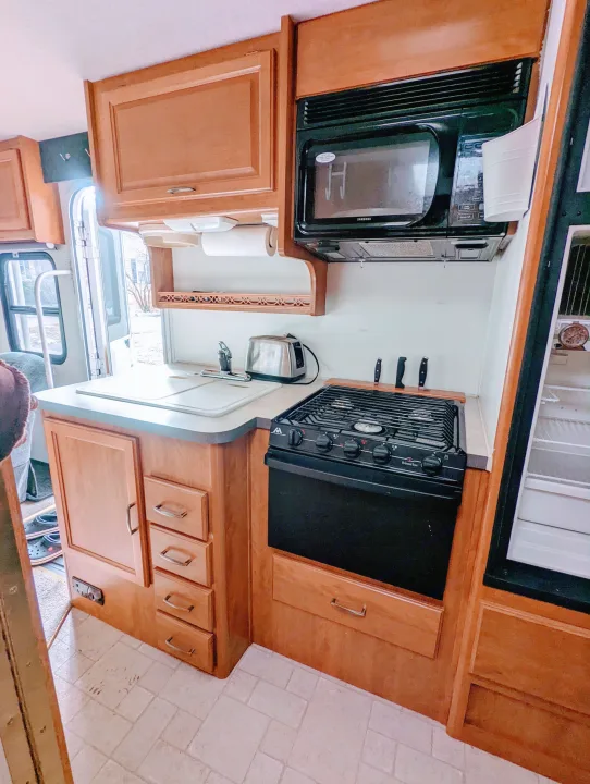 Compact RV rental kitchen with microwave, stove, sink, and cabinets. Perfect for mobile cooking.. Fleetwood Tioga 2005