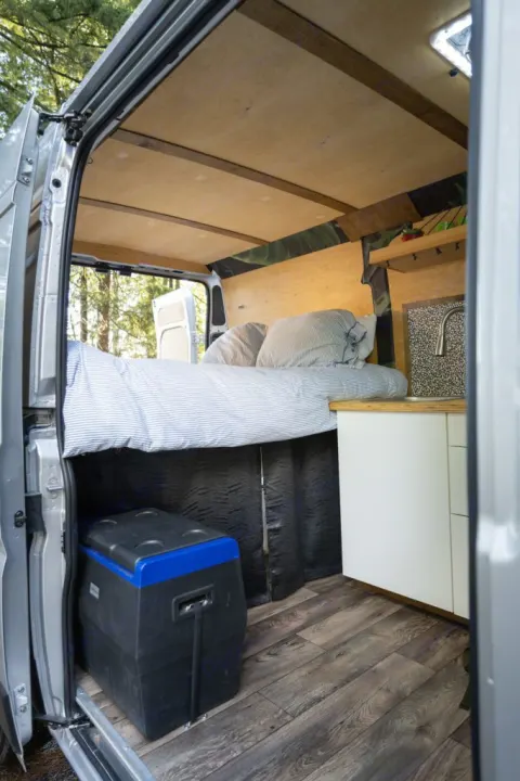 Cozy RV rental camper van interior with bed, cooler, & compact kitchen. Perfect for mobile living & road trips.. RAM ProMaster 2021