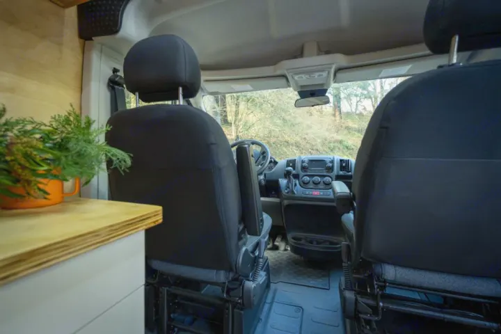 RV rental van interior: From the back, see front seats, cockpit, and dashboard. A plant on a counter suggests the living space.. RAM ProMaster 2021