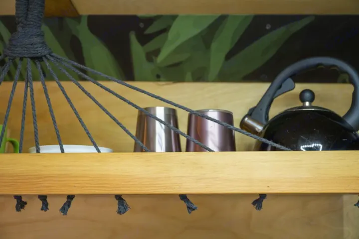 Organized RV rental camper van kitchen shelf with kettle, cups, and a rope storage hammock above.. RAM ProMaster 2021