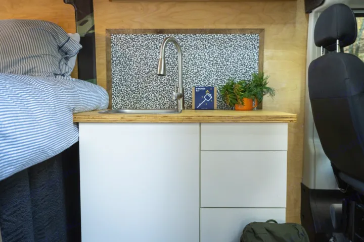 Cozy RV rental interior with a compact kitchen, sink, bed, and stylish wood accents. Perfect for adventure!. RAM ProMaster 2021