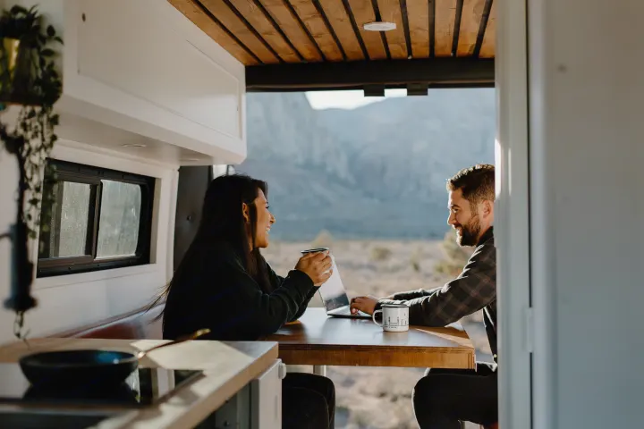 A couple works and drinks coffee inside a modern RV rental, enjoying scenic mountain views. Ideal for remote work travel.. Dodge Sprinter 2019