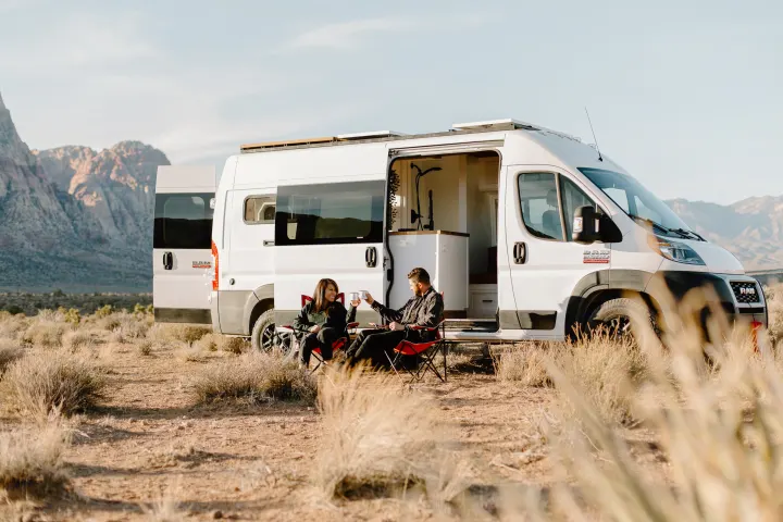RV rental adventure: Couple relaxing outside their camper van in a scenic desert mountain landscape.. Dodge Sprinter 2019