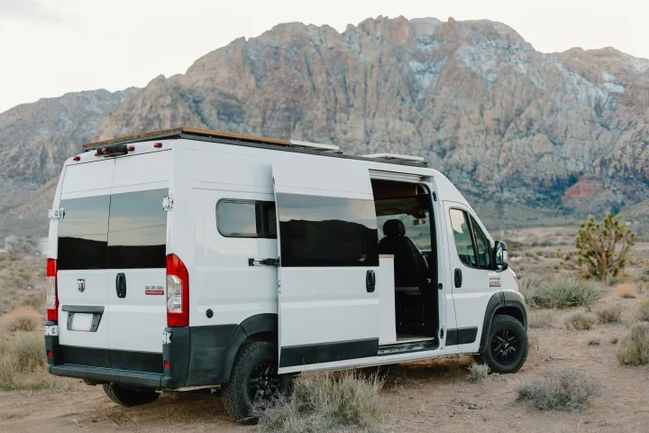 Spacious white RV rental camper van with open side door in a scenic desert mountain landscape, perfect for your next road trip.. Dodge Sprinter 2019
