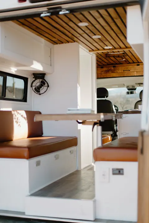 Interior of a modern rv rental featuring a custom wood-slat ceiling, brown leatherette benches, and a dining area.. Dodge Sprinter 2019