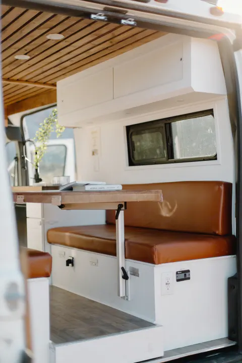 Cozy RV rental interior: wood-slat ceiling, comfy dinette with a fold-down table, kitchen, & power.. Dodge Sprinter 2019