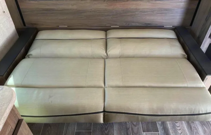 RV rental interior: A beige convertible sofa bed with dark trim and wood paneling, ready for relaxation or sleep.. Gulf Stream Enlighten 2022