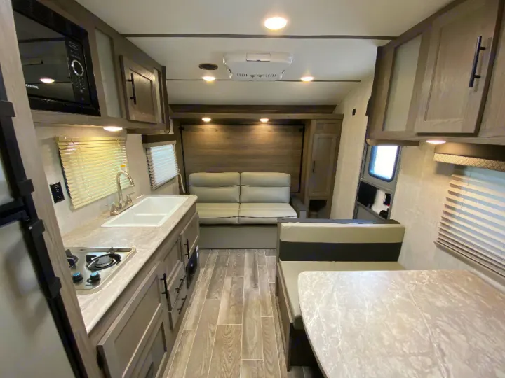 RV rental interior showcasing a compact kitchen with sink and stove, a dinette, and a sofa/bed lounge area.. Gulf Stream Enlighten 2022