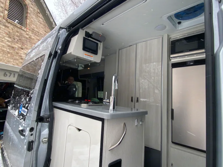 Step inside this RV rental! A compact kitchen with sink, stovetop, microwave, and fridge, ready for snowy adventures.. Thor Sprinter 2022