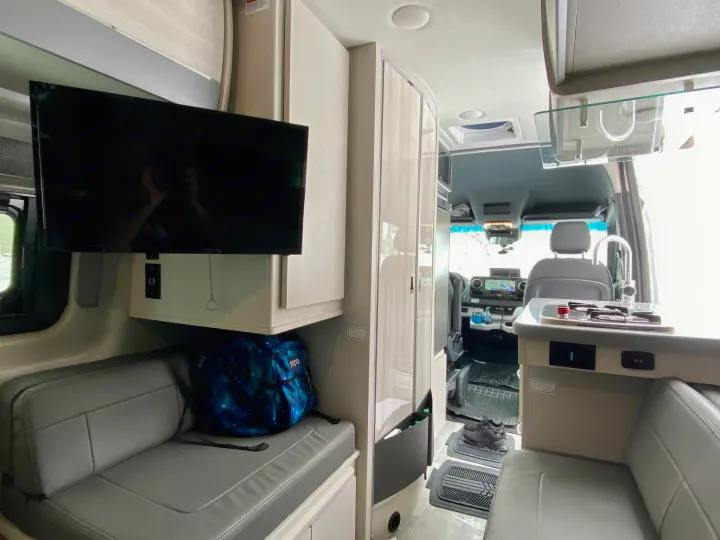 An RV rental's interior, featuring a TV, seating, and kitchenette with a view to the front cabin.. Thor Sprinter 2022