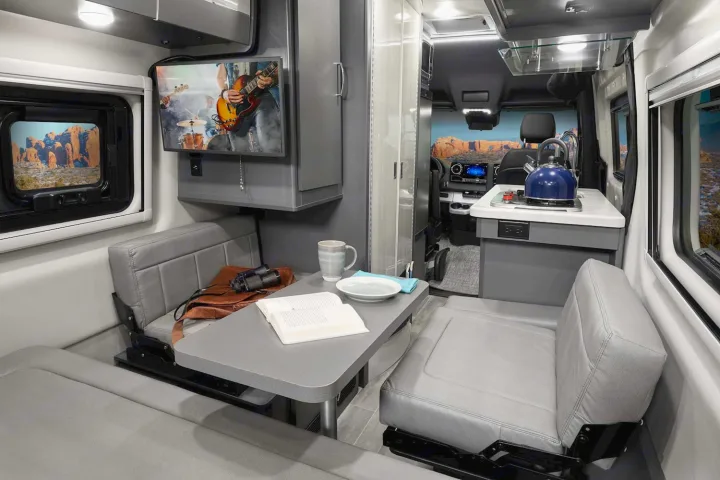 Comfortable RV rental interior showing a dining nook with TV & kitchen. Ready for scenic adventures on the road!. Thor Sprinter 2022