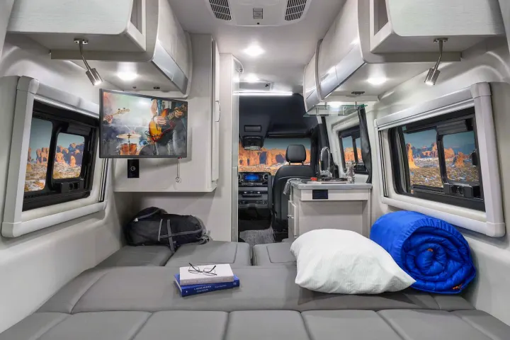 Modern RV rental interior: cozy bed, TV, kitchen, and scenic desert views. Ideal for comfortable adventure travel.. Thor Sprinter 2022