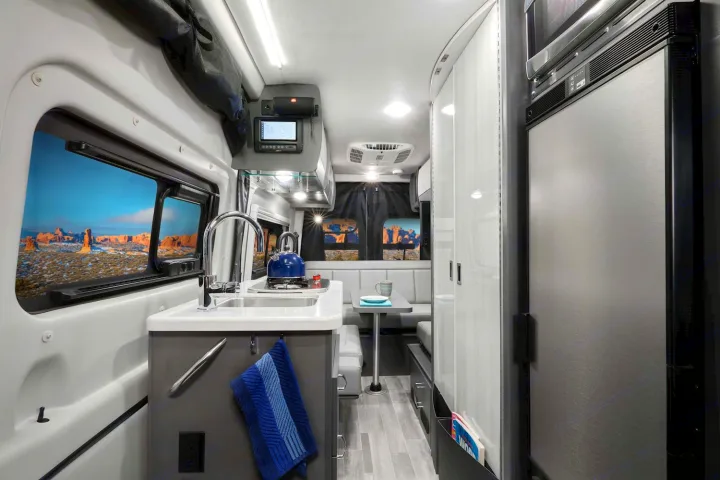 Inside a modern **rv rental**: a compact kitchen with sink & stove, dining space, and panoramic desert views. Ideal for mobile living & travel.. Thor Sprinter 2022