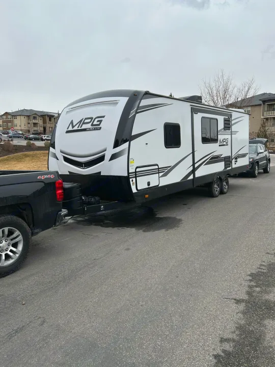 Black pickup truck tows a white 'MPG ULTRA-LITE' travel trailer on a street. Ideal RV rental for adventures.. Cruiser RV MPG Ultra Lite 2500BH 2021