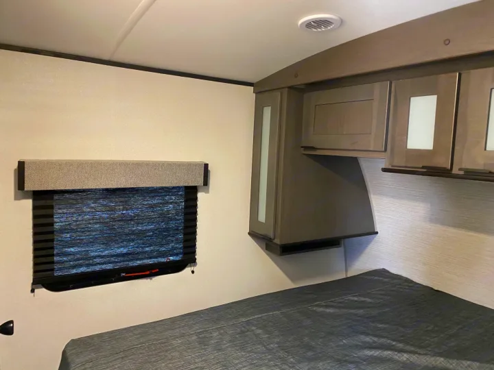 Cozy RV bedroom interior featuring a comfortable bed, window with blinds, and overhead cabinets for your RV rental.. Cruiser RV MPG Ultra Lite 2500BH 2021