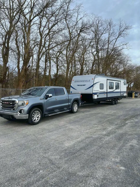 Grey GMC truck towing a white Springdale travel trailer, ready for your next RV rental experience.. Keystone RV Springdale 2021
