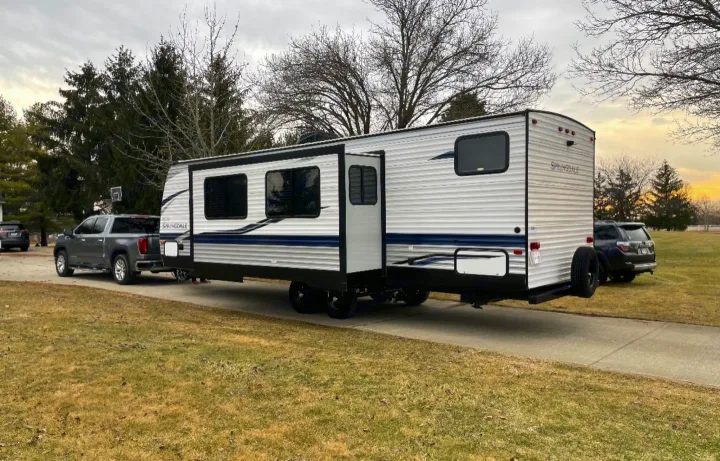 Large travel trailer, perfect for an **RV rental** trip, hitched to a pickup truck on a driveway, ready for camping adventures.. Keystone RV Springdale 2021