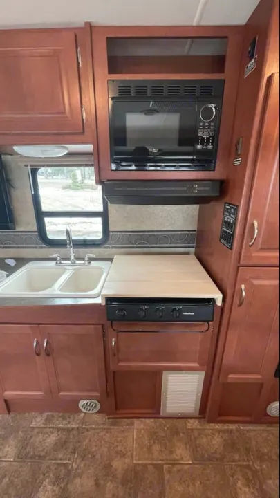 RV rental kitchen showcasing a microwave, stovetop, double sink, and ample wood cabinetry. Perfect for travel.. Winnebago Minnie Winnie 2014