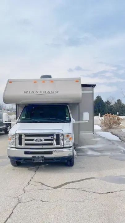Front view of a white Winnebago Class C motorhome, ideal for an rv rental, parked on cracked asphalt under a cloudy sky.. Winnebago Minnie Winnie 2014