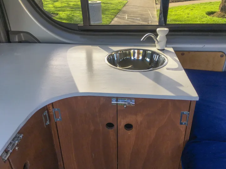 This RV rental's interior features a compact kitchenette with a stainless steel sink, white faucet, and wooden cabinets.. Toyota Hiace 2009