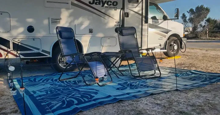 An RV rental provides a cozy outdoor setup: two zero-gravity chairs on a blue mat, ready for relaxation.. Jayco Redhawk 2020