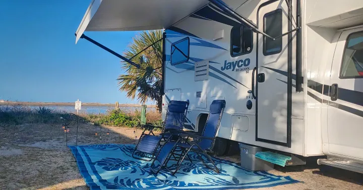 RV rental at a scenic waterfront campsite with a Jayco RV, awning, chairs, and outdoor lights.. Jayco Redhawk 2020