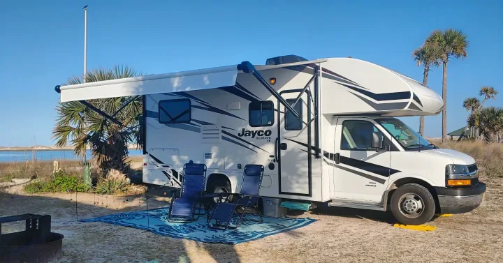 Serene RV rental camping by the beach. A Jayco motorhome with extended awning, chairs, and fire pit ready for relaxation.. Jayco Redhawk 2020